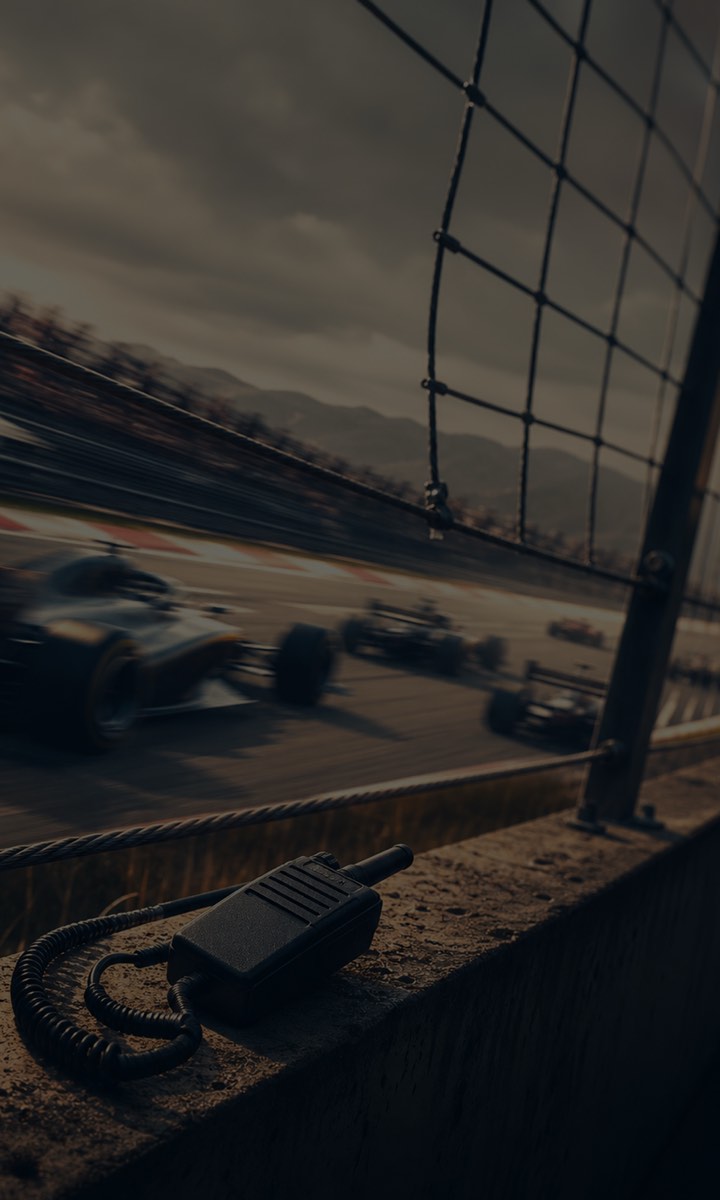 Racing cars pass the pit wall, with a team radio in the foreground